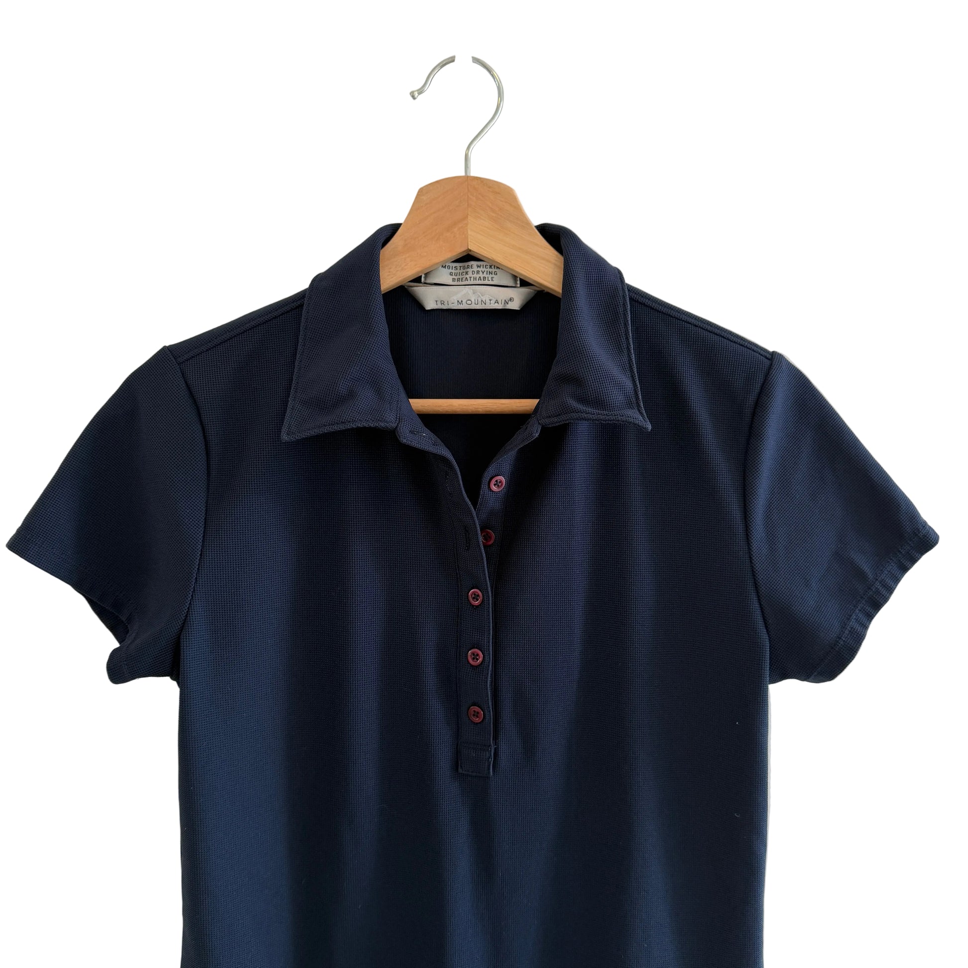 Navy blue polo shirt on a wooden hanger against a white wall