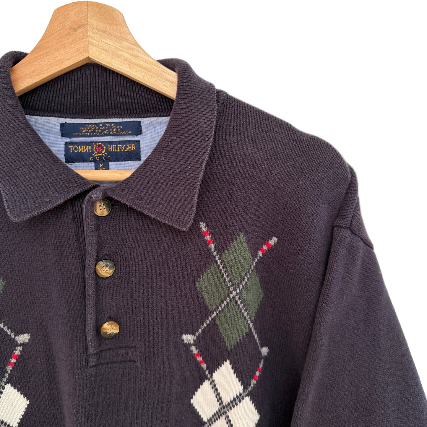 Navy argyle sweater with buttons on a hanger against a light background
